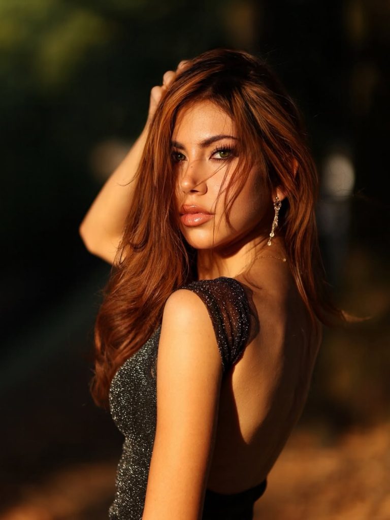 Modella con capelli lunghi e brillanti in un abito scintillante, sexy e elegante, scattata nel parco.